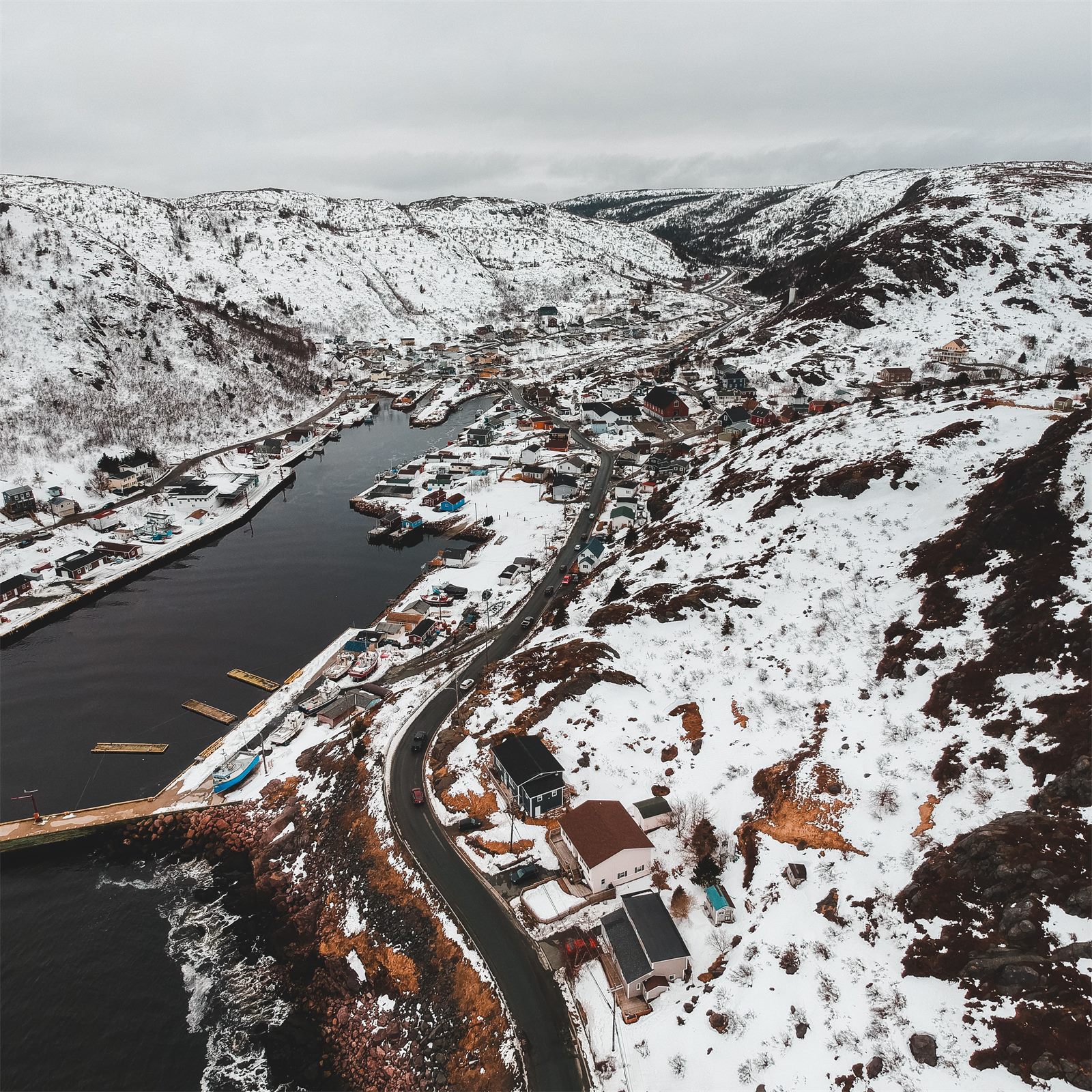 Aerial view of a remote northern community, homes and a small harbour tucked between snow-covered hills along the coast
